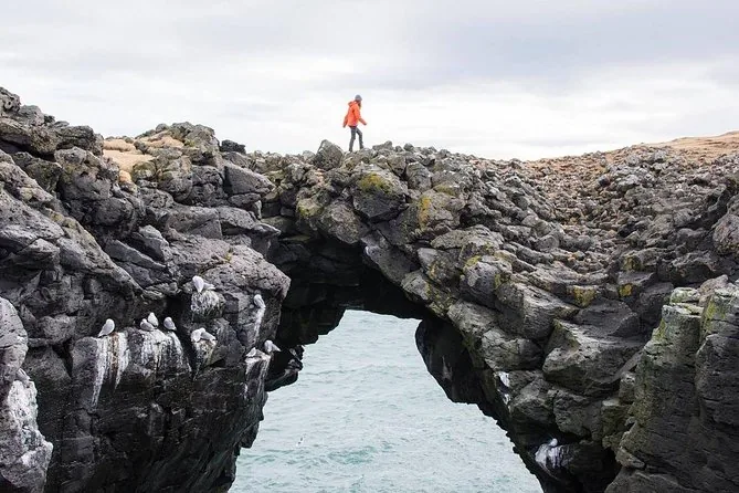 A walker standing on a natural rock arch above the sea
