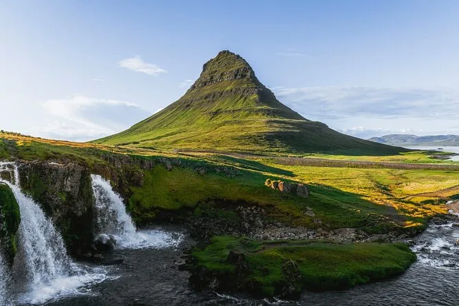 Kirkjufell above green slopes and a waterfall in summer